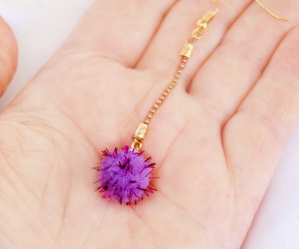 purple pompom earring on a hand