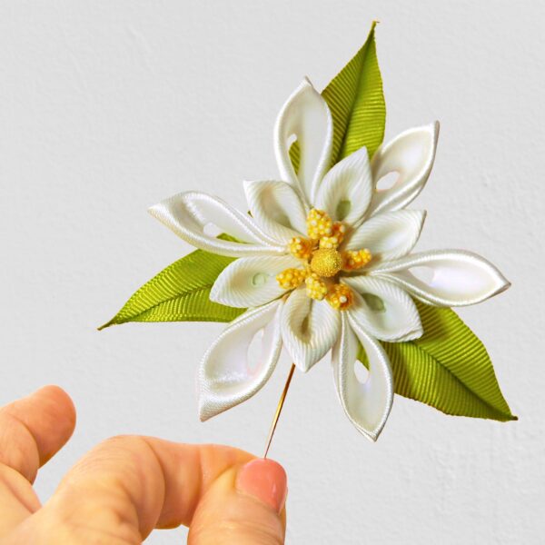 White flower with yellow stems brooch in a hand